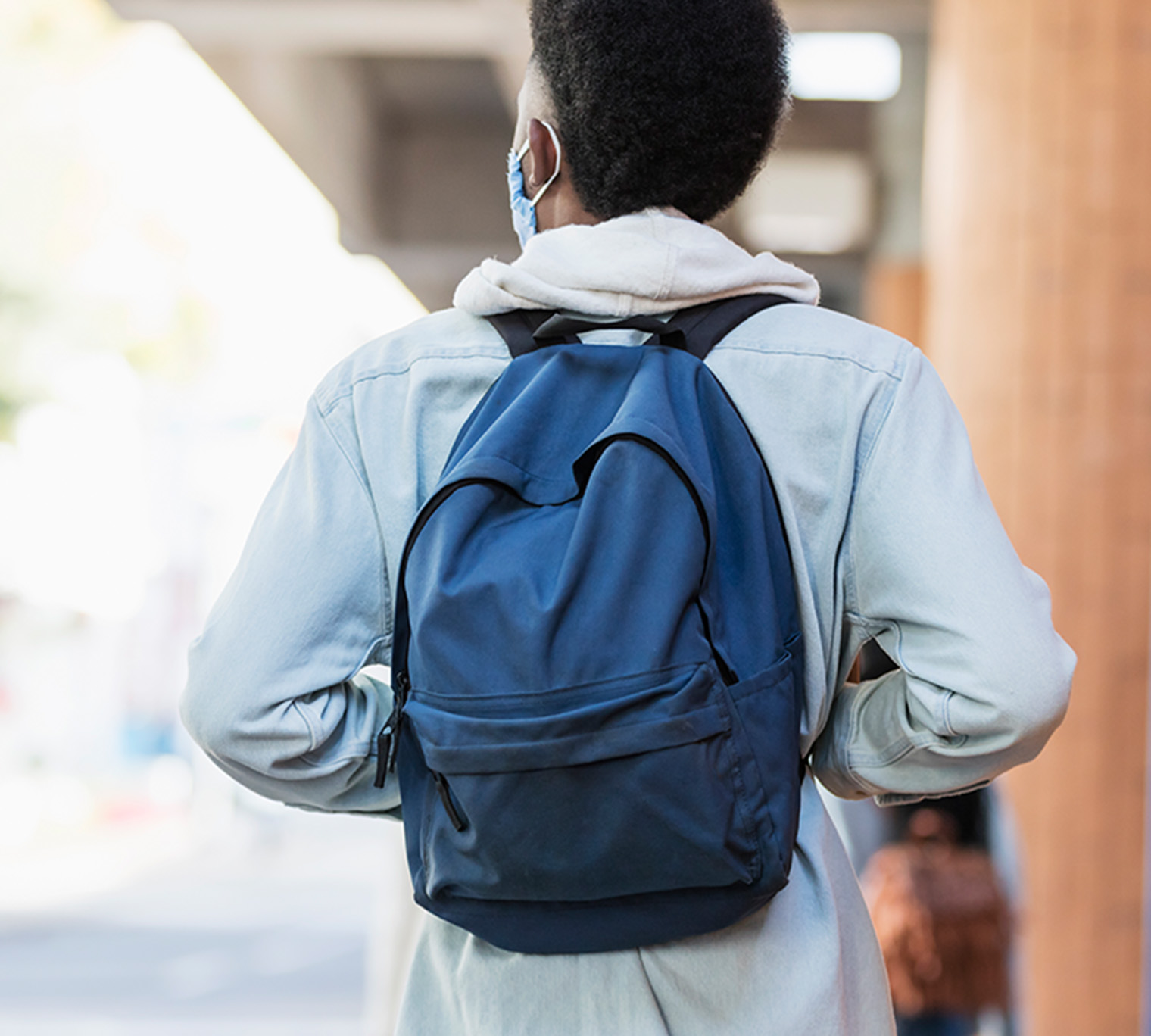 boy in a mask with a backpack on walking outside the school