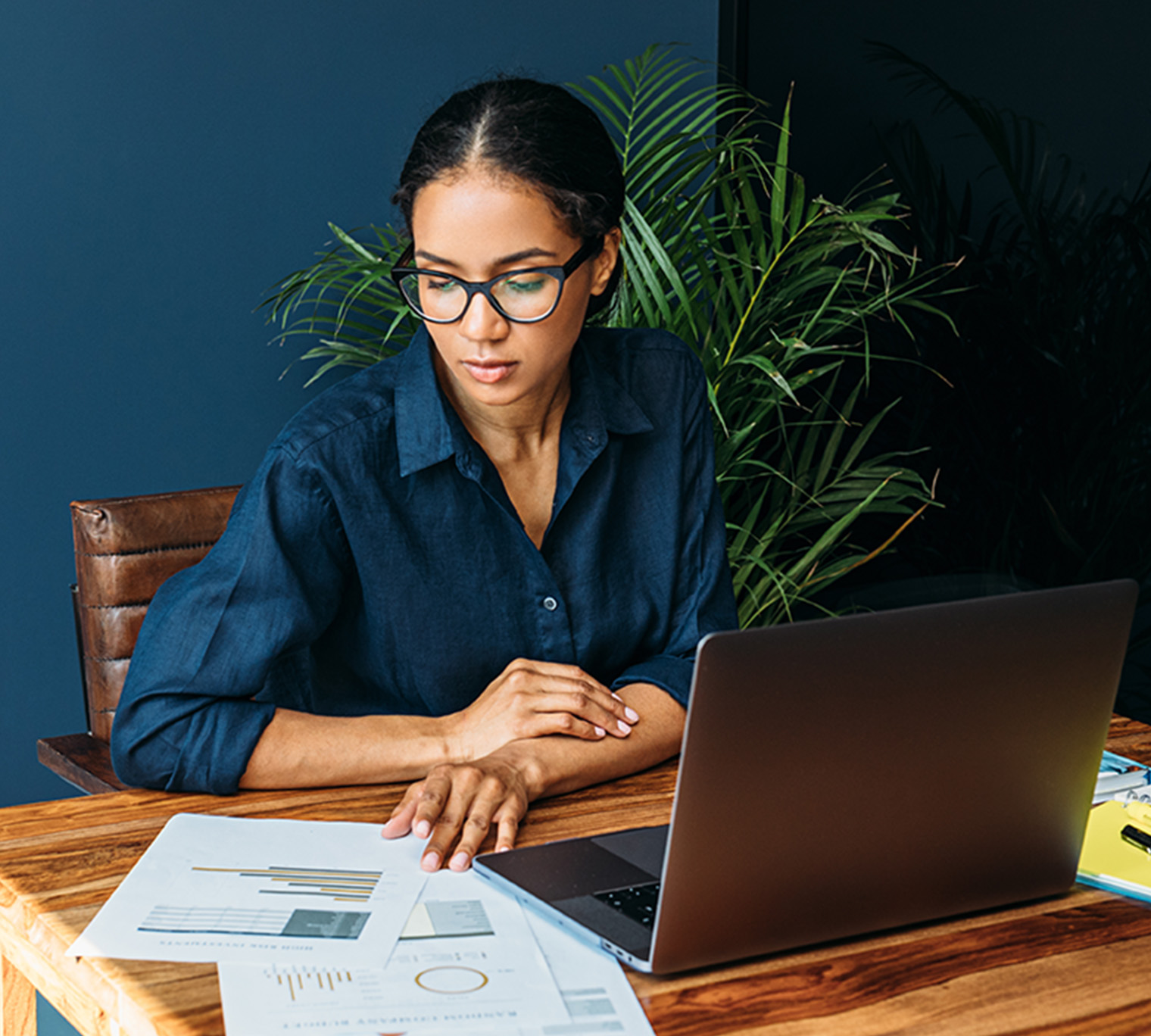 person focused on papers sitting at a desk with their laptop open