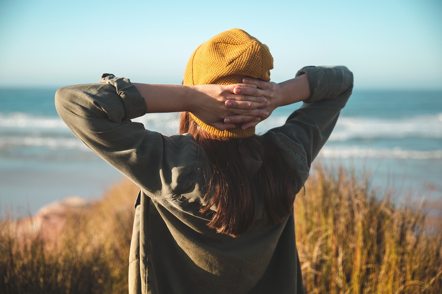 Woman with hands behind her head looking out to the ocean