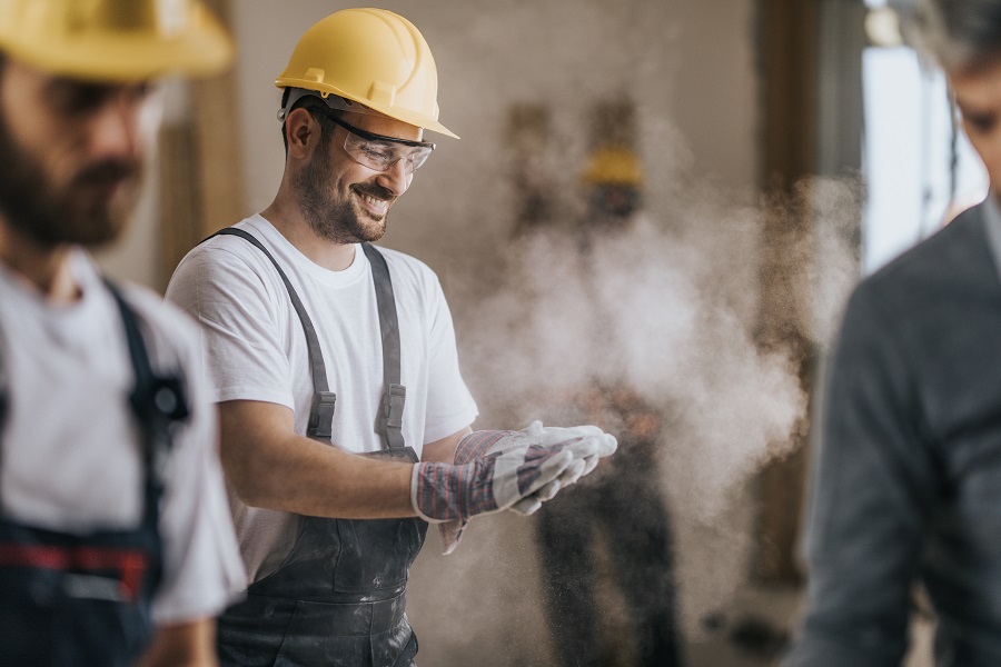 Happy construction worker cleaning his gloves from sawdust at in renovating apartment.