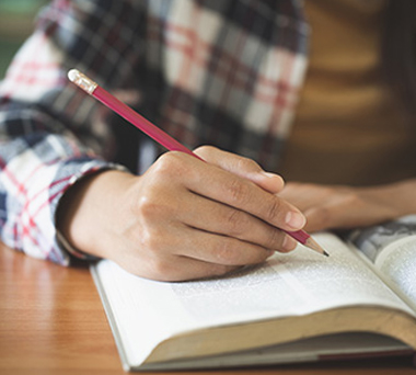 Handing holding pencil over open book