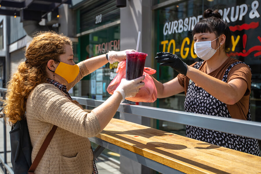 Masked woman getting food from masked worker