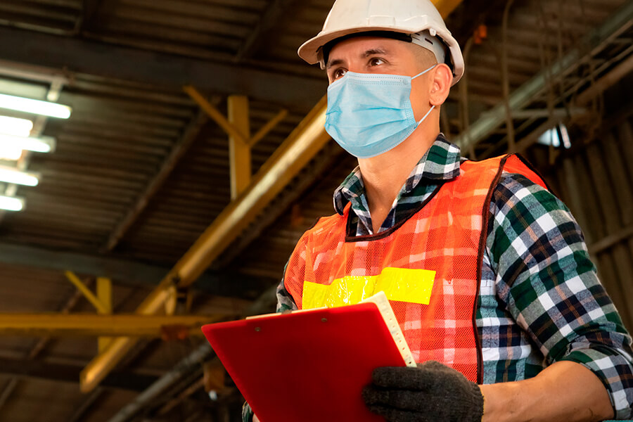 Masked man wearing safety gear holding clipboard