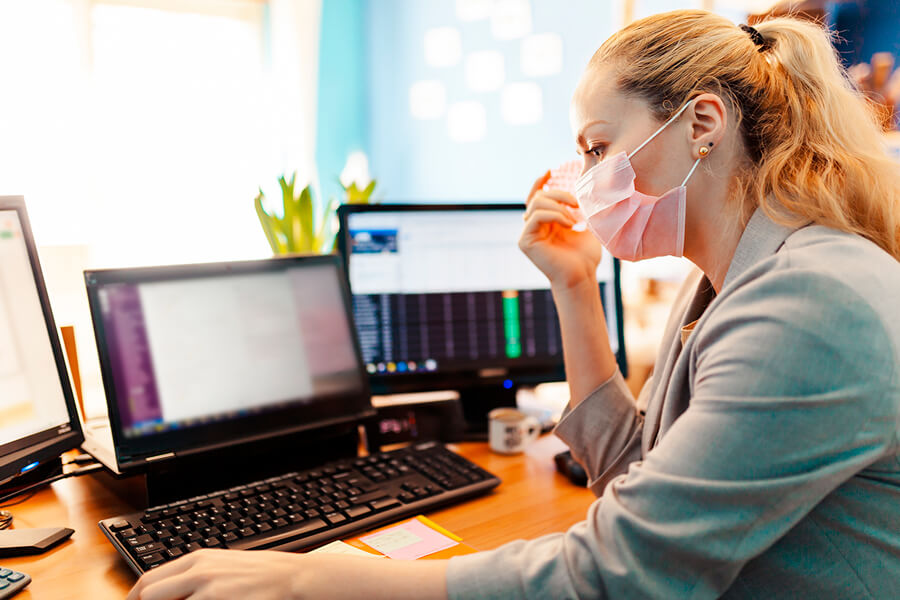 Masked woman working on computers in an office
