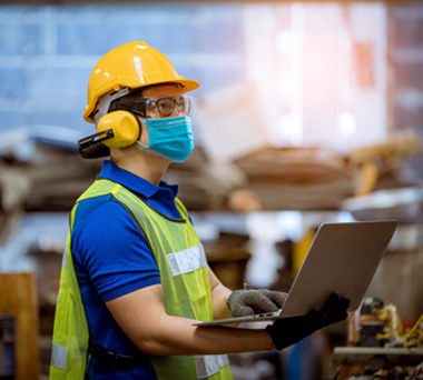 Worker in safety gear and laptop at a construction site