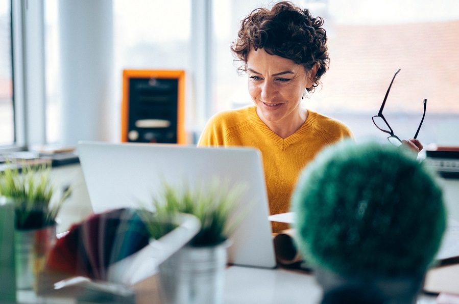 Smiling woman holding glasses in front of laptop