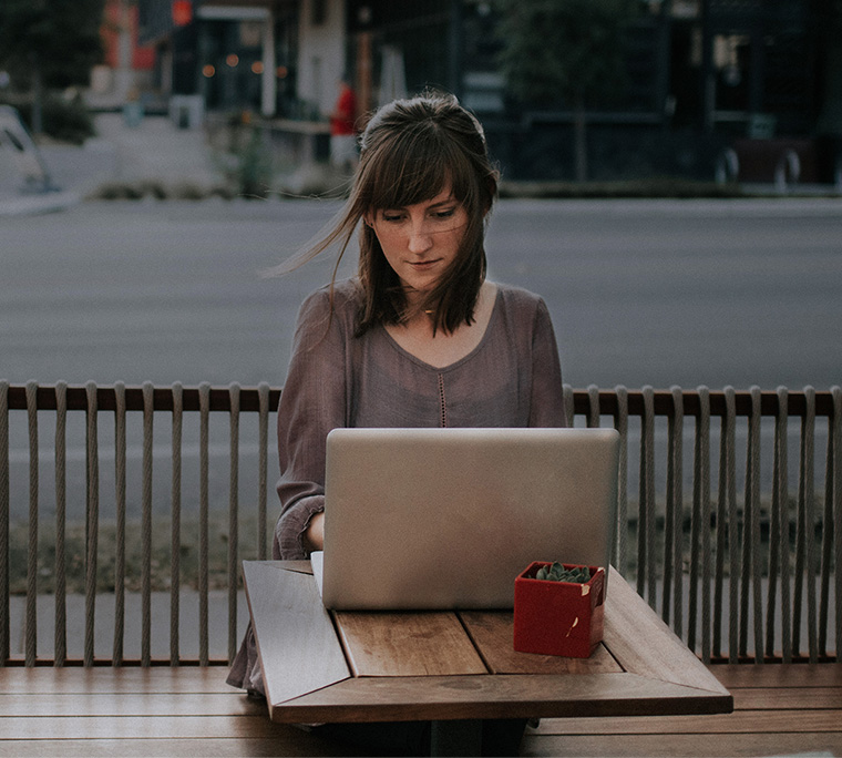 Person working on laptop sitting at café patio.