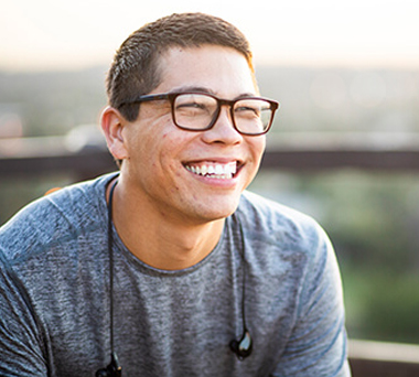 Smiling man with ear buds around neck out of doors
