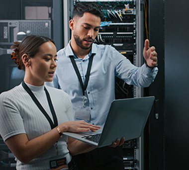 Two people working on laptop in server room