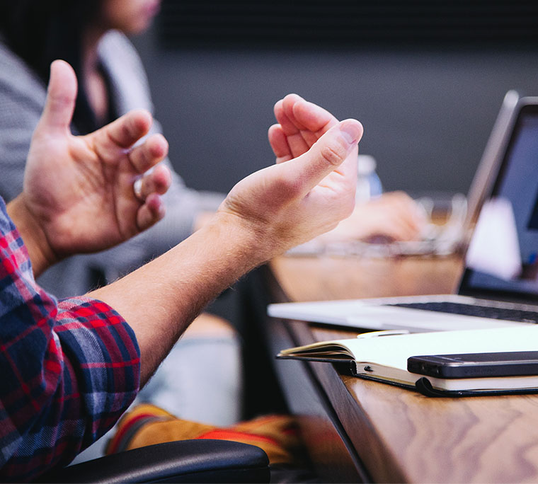 Conversational hands at a table with a laptop and a notebook.
