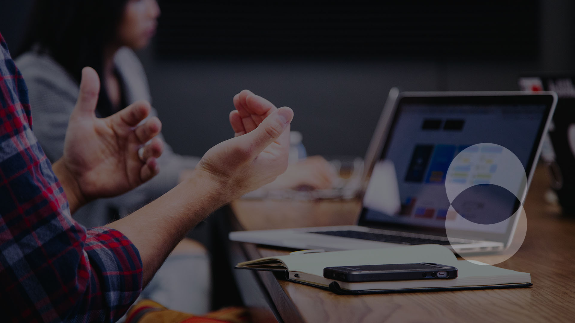 close up of hands, implying the person is engaged in a conversation. they are sat in front of the a Signal49 Research table with a laptop, notebook and a smartphone.
