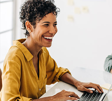 Person wearing a big smile working on laptop.