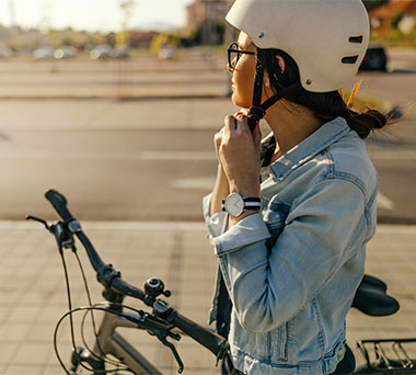 Person standing over their bicycle getting their helmet clipped on.
