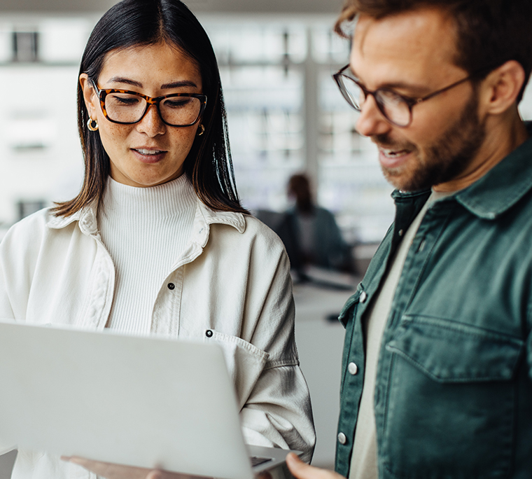 Woman and man in office, looking at laptop, discussing survey