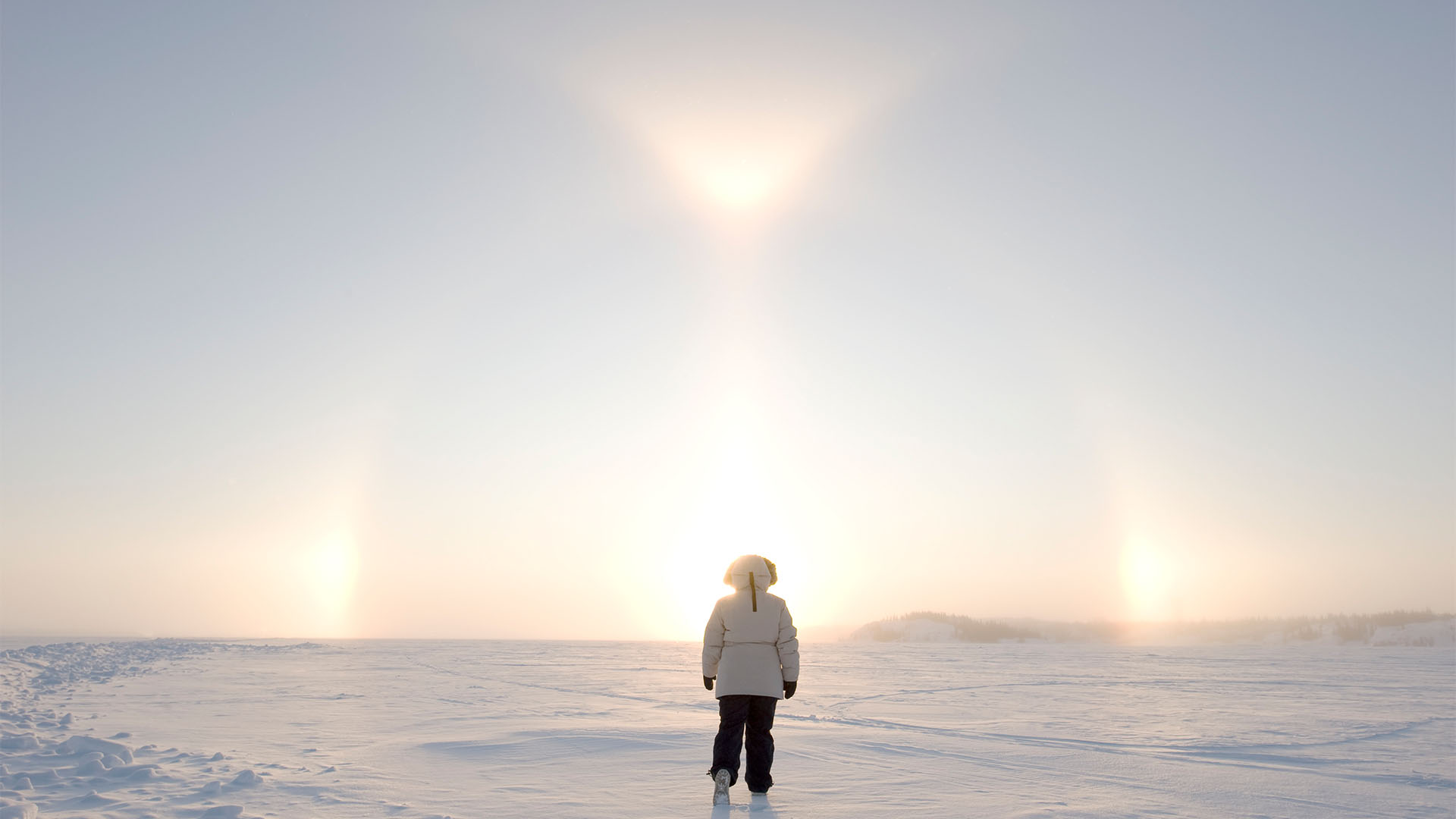 Person in full snow suit walking out across flat land covered in snow.