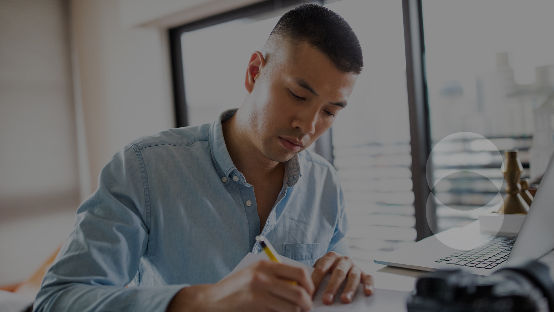 Person at their desk taking notes with their laptop open next to them.