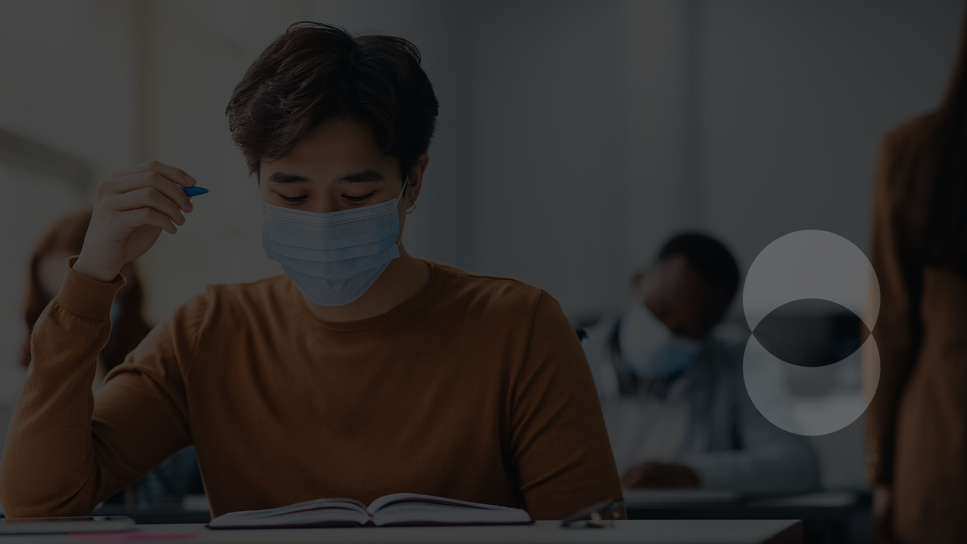Man wearing mask in a classroom working in a notebook.