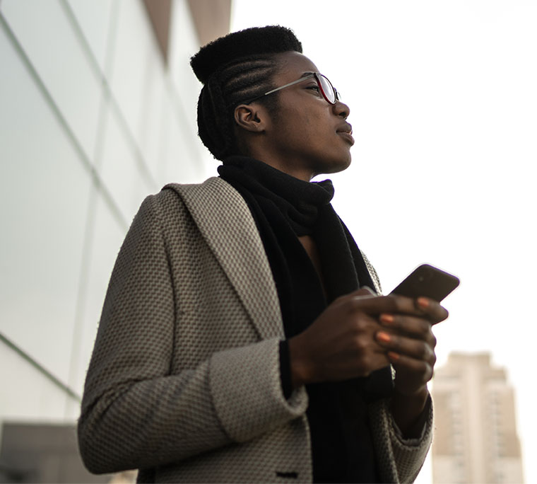 person holding a cellphone looking out into the distance in front of a large windowed building
