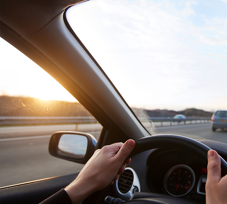a close-up of hands holding a steering wheel, driving down the highway