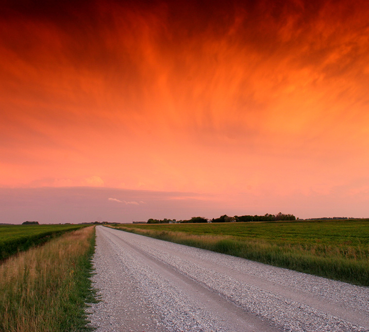 an orange sunsets at the end of a dusty farm road
