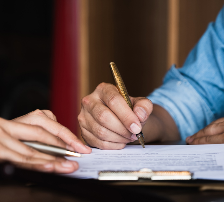 Close-up shot of hand holding pen signing papers