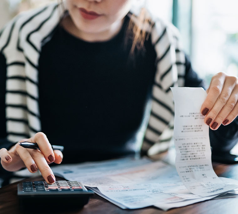 Woman managing personal banking and finance at home at the table with a calculator, a pen and receipts.