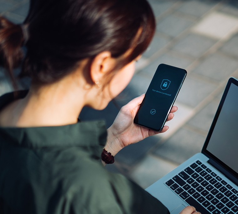 Businesswoman logging in to laptop and holding smartphone with a security key lock icon on the screen