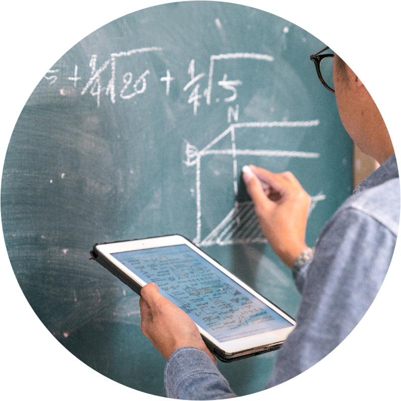 Close-up of professor writing on chalkboard holding tablet
