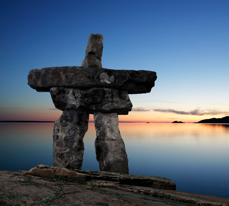 Inukshuk with still river in background at dusk