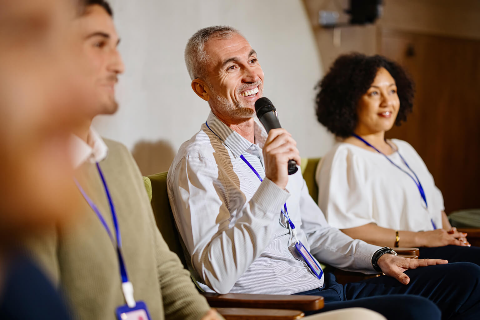 Smiling white man holding a microphone while sitting with 2 other men and woman