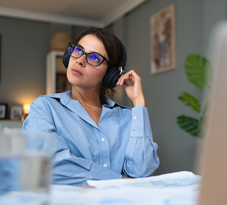 woman staring off into the distance in front of her work station while wearing headphones