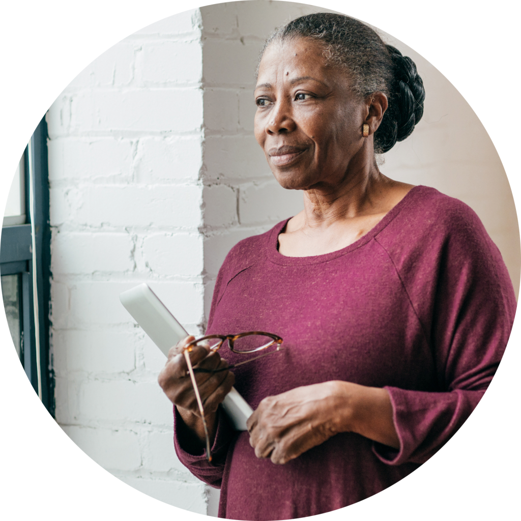 Senior woman holding tablet and glasses, looking out window