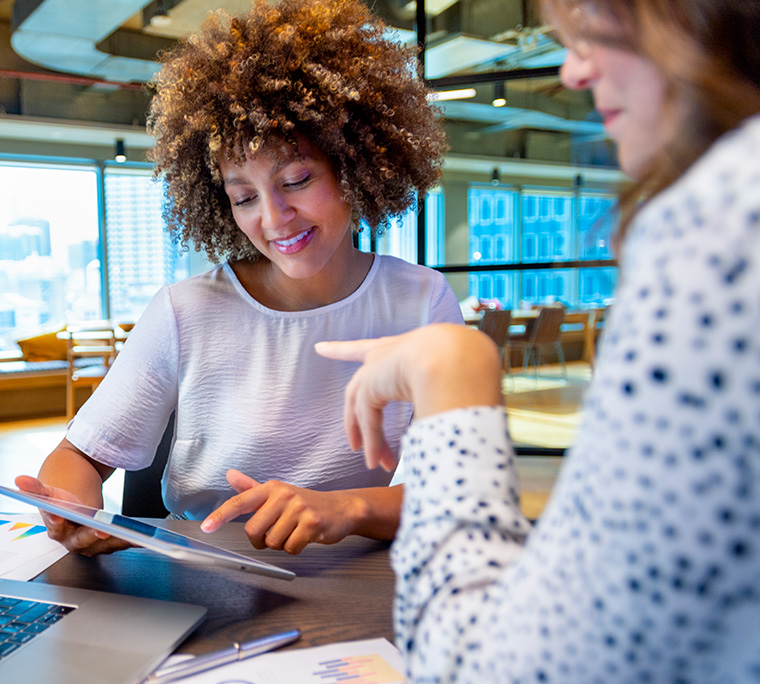 two women are looking at a tablet in an office meeting